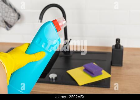 Housekeepers hand holding cleaning supplies in front of black kitchen sink Stock Photo