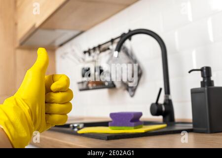 Housekeepers hand holding cleaning supplies in front of black kitchen sink Stock Photo