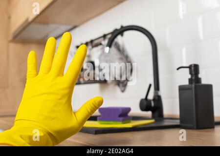 Housekeepers hand holding cleaning supplies in front of black kitchen sink Stock Photo