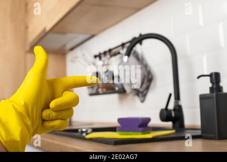 Housekeepers hand holding cleaning supplies in front of black kitchen sink Stock Photo