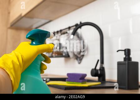 Housekeepers hand holding cleaning supplies in front of black kitchen sink Stock Photo