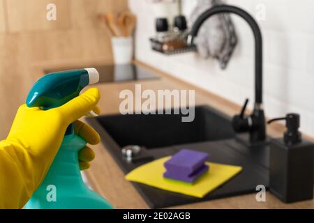 Housekeepers hand holding cleaning supplies in front of black kitchen sink Stock Photo