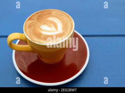 Closeup of cappuccino coffee in yellow brown cup isolated on blue wooden table Stock Photo