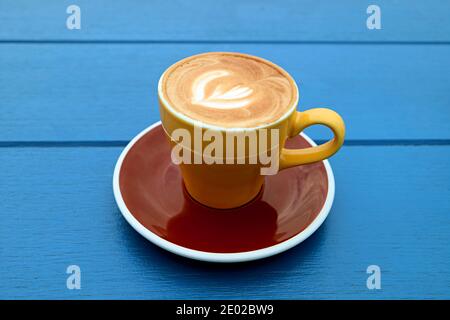 Cappuccino coffee in yellow brown cup isolated on blue wooden table Stock Photo