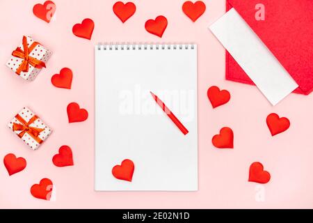 Flatlay notepad mock up with felt-tip pen with a red envelope with hearts and gifts on a pink background. Concept of valentine's day and writing love Stock Photo