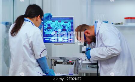 Team of experienced biologists working on microscopes in modern equipped laboratory. Scientists stuff examining vaccine evolution using high tech researching diagnosis against covid19 virus Stock Photo