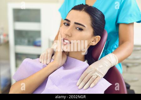 Woman patient feeling toothache touching cheek in dental clinic