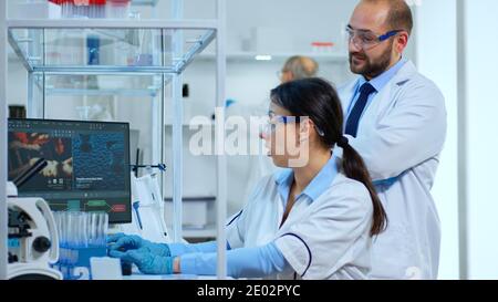 Research scientists working on pc with medical equipment analyzing blood and genetic material samples with special program in modern equipped laboratory. Multiethnic team examining virus evolution Stock Photo