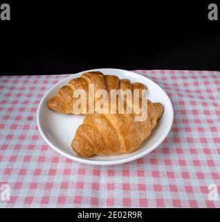 Delicious fresh croissants in plate on pink Plaid pattern background. French breakfast. Tasty croissants with copy space Stock Photo