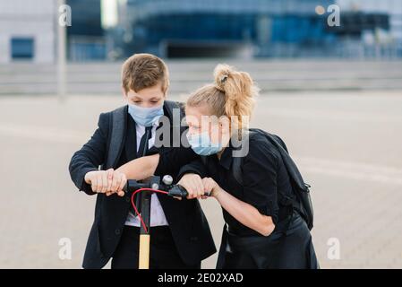 Education, childhood and people concept. Happy school children with backpacks and scooters outdoors in protective mask Stock Photo