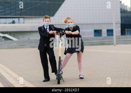 Education, childhood and people concept. Happy school children with backpacks and scooters outdoors in protective mask Stock Photo