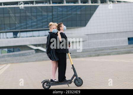 Education, childhood and people concept. Happy school children with backpacks and scooters outdoors in protective mask Stock Photo