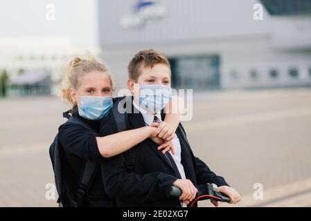 Education, childhood and people concept. Happy school children with backpacks and scooters outdoors in protective mask Stock Photo