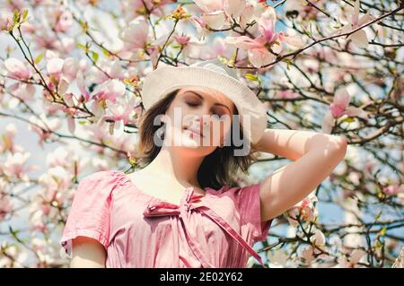Portrait of young attractive woman in spring garden with blooming magnolias. Spring background. Woman's Day. Greeting card. Stock Photo