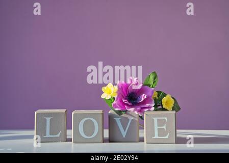 LOVE message spelled in four wooden blocks under colourful flowers. Blessings and gifts for family and friends during coronavirus epidemic period. Stock Photo