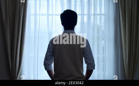 Back view of confident young thinking businessman standing before bright window indoors Stock Photo