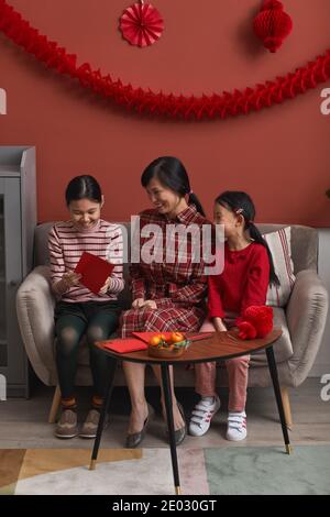 Vertical long shot of modern Chinese family consisting of mother and two daughters spending time together preparing for New Year holidays Stock Photo