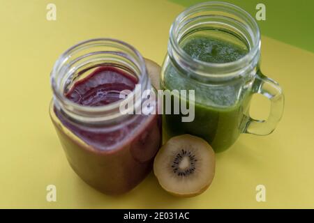 Smoothies with fresh kiwis.Healthy green and red detox drinks in mason jar on yellow background. Stock Photo