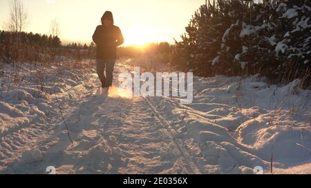 Walk the Snow Trail to Sunset. Man Walks in the Snow in Backlit Sunlight Stock Photo
