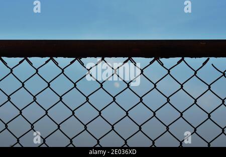 full moon behind iron wire fence on bright sky in evening Stock Photo