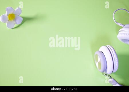 Frangipani and white headset lying flat on green pastel background, copy space Stock Photo