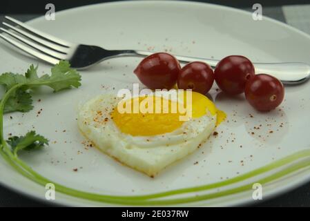 Closeup of heart-shaped fried egg, cherry tomatoes in white porcelain plate, nutrient breakfast Stock Photo