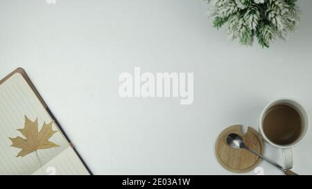 Creative layout. Coffee in a white cup, spoon on a wooden saucer, maple leaf specimen on open notebook. Top view of desk. Copy space Stock Photo