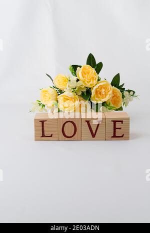 Love message written in wooden blocks. Yellow artificial rose decoration, white background with copy space, text on wooden cubes. Vertical image Stock Photo