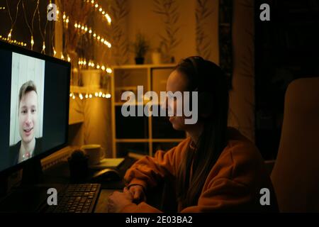 Long distance video call, man and woman using videoconference application for virtual communication, online meeting, side view. Dark, festive home atm Stock Photo