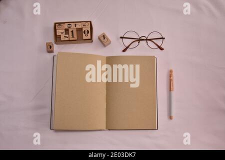 Open brown notebook, pen, glasses, wooden squares lying flat on desk, top view, copy space Stock Photo