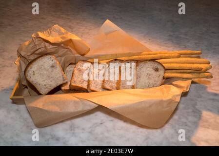 Bread with walnuts, slices of loaf on breadsticks in brown bakery paper on a marble surface Stock Photo