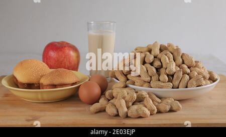 Healthy breakfast, plate of peanuts, two eggs, glass of milk, two cakes and an apple in kitchen Stock Photo