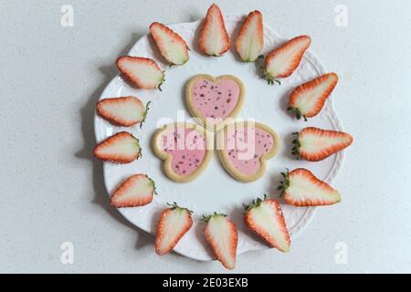 Heart-shaped cookies, cut strawberries making a circle on a plate, top view Stock Photo