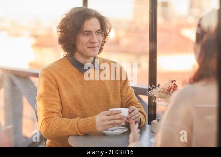 Young man drinking tea during conversation with his friend at meeting in cafe Stock Photo