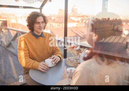 Young couple sitting at the table with cups of tea and talking to each other during their meeting in cafe Stock Photo