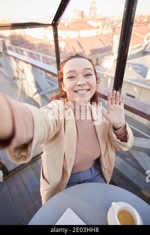 Young woman smiling at camera making selfie portrait on her mobile phone while standing at the restaurant Stock Photo