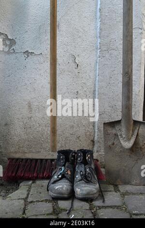 old worn painted work boots with a yard broom and a spade as symbol for cleaning, house keeper or maintenance Stock Photo