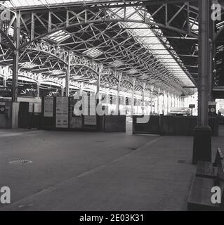 1966, historical, an empty Marylebone railway station, London, England, UK, showing gates for freight to enter the platforms and advertising posters of the day. One poster advertises the film, 'The Glass Bottom Boat', another the Evening News paper. Also seen is the intricate ironwork of the concourse roof. The station opened in 1899 as the London terminus of the Great Central Main Line (GCML), the last major railway to have been built in Britain. The railway line connected London with the northern cities of Sheffield and Manchester. Stock Photo