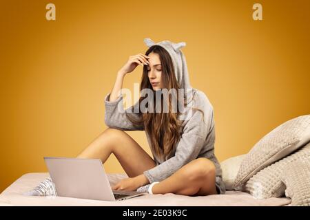 Attractive young woman wearing kigurumi pajamas, is upset in front of her laptop Stock Photo