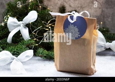 Gift in a bag made of kraft paper, against the background of a spruce wreath and garland. Stock Photo