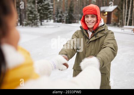 Happy young man in warm clothing holding hands with his girlfriend while they walking outdoors in winter Stock Photo