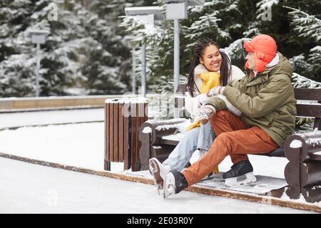 Young happy couple talking to each other while sitting on bench outdoors in winter park Stock Photo