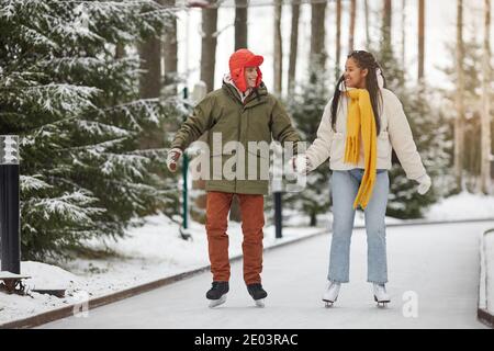Happy couple holding hands and smiling to each other while skating in the park Stock Photo