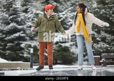 Two friends in warm clothing enjoying the leisure time outdoors skating on skating rink Stock Photo
