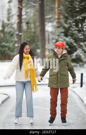 Young couple skating together holding hands and talking in outdoor skating rink Stock Photo