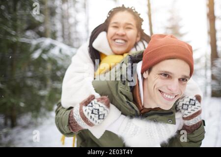 Happy couple having fun outdoors man riding his girlfriend on his back they walking in winter forest Stock Photo