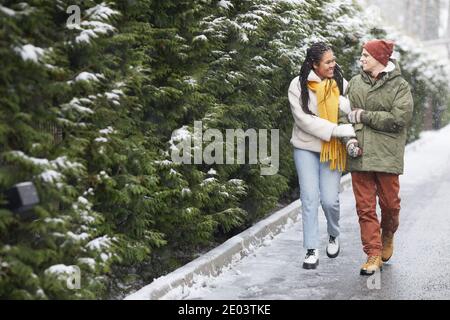 Happy loving couple in warm clothing walking along the path in the park during snowy weather Stock Photo