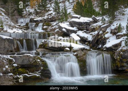 river going through snowy valley in rock waterfalls with snowy trees Stock Photo