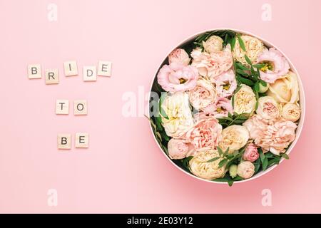 Bride to be lettering on the wooden squares with letters on the pink background and big round box with red flowers and roses. Stock Photo
