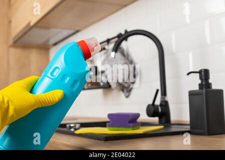 Housekeepers hand holding cleaning supplies in front of black kitchen sink Stock Photo